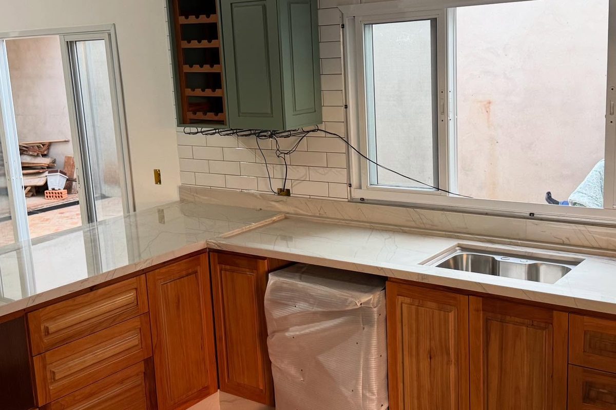 Cozinha em L com bancada em pedra clara e marcenaria em madeira